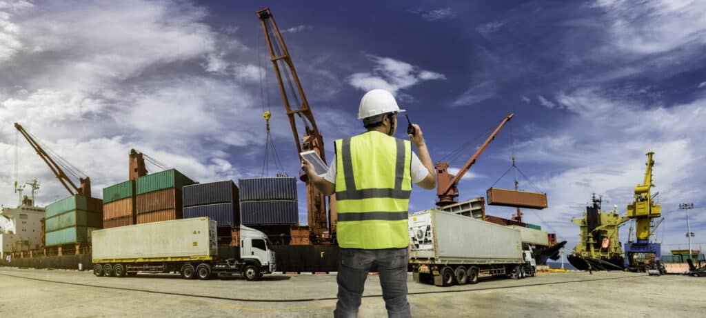 Freight forwarding worker overseeing containers at a busy shipping port.