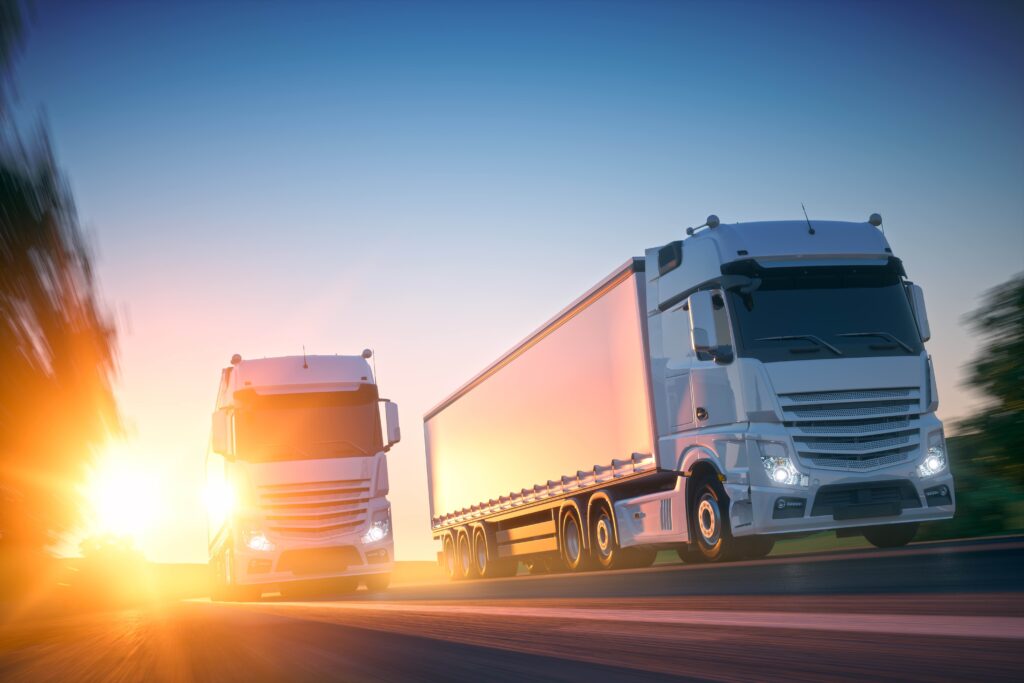 Freight trucks driving in convoy on the highway at sunset.