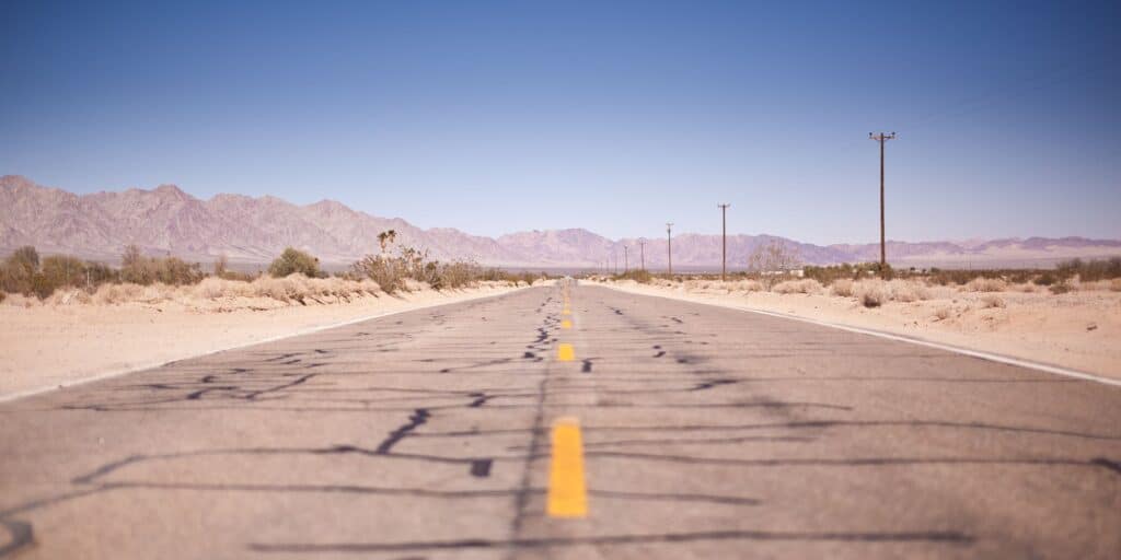 Empty desert highway stretching toward distant mountains under a clear sky.
