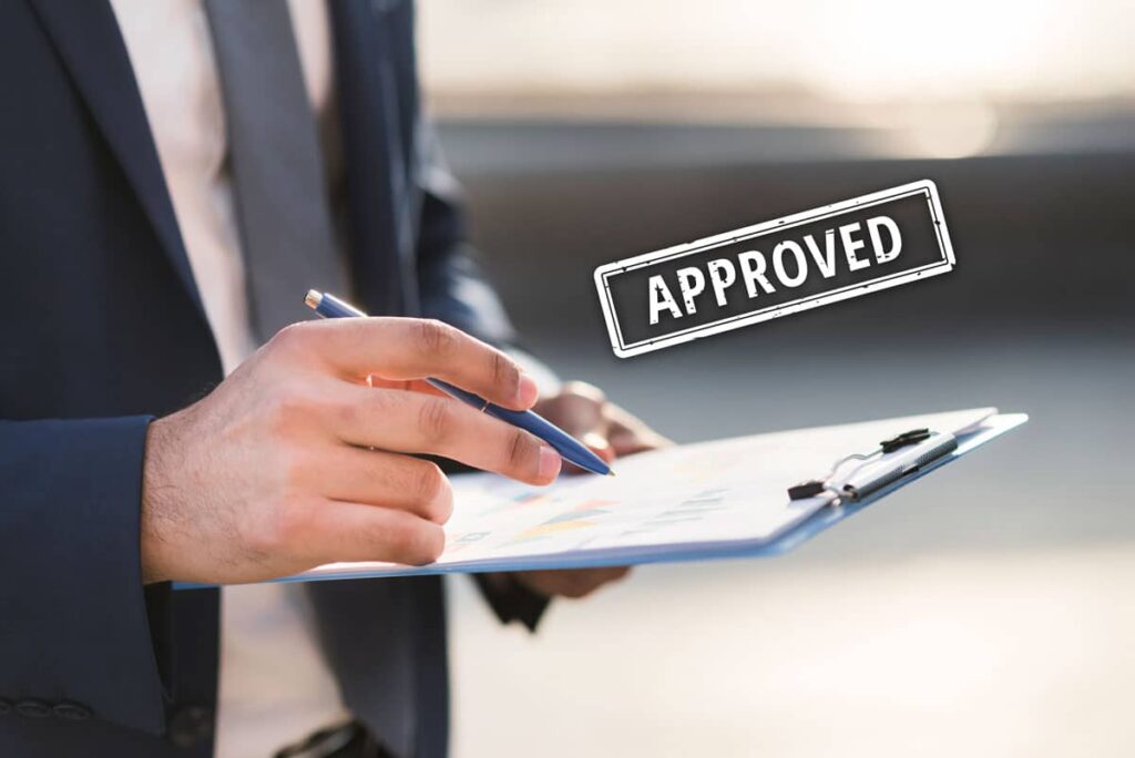 Approved stamp over businessman reviewing paperwork on a clipboard.