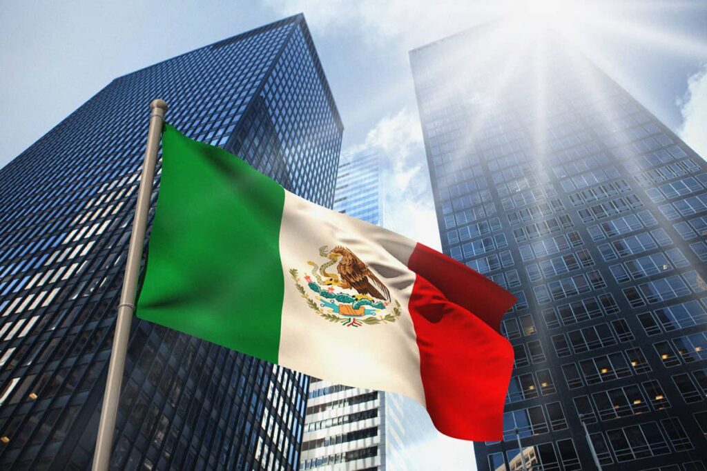 Mexican flag waving between glass skyscrapers under bright sunlight