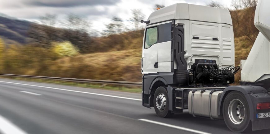White semi truck cab driving on a highway with blurred hills in the background.